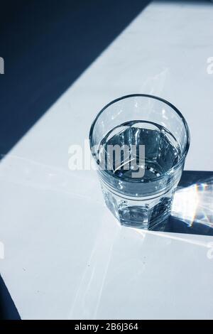Vetro d'acqua con forti ombre su sfondo bianco, tonalità blu classico del 2020 Foto Stock