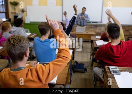 Vista posteriore degli studenti che alzano le mani in classe Foto Stock