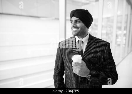 Felice giovane e bello indiano Sikh uomo d'affari che guarda attraverso la finestra Foto Stock