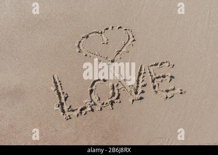 Simbolo di cuore disegnato e amore di parola scritto nella sabbia della spiaggia Foto Stock
