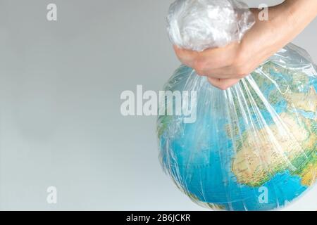 La mano umana tiene la terra in cattività. Globo in un sacchetto di plastica bianco. Il concetto di disastro ambientale su un fondo bianco isolato Foto Stock