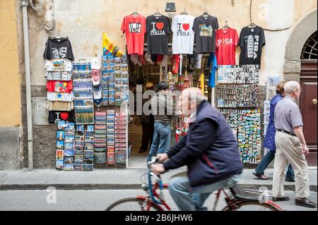 PISA, ITALIA - 23 MAGGIO 2012: Un ciclista italiano passa per uno stand di souvenir che vende magliette e bacchette su una strada che conduce alla Torre Pendente. Foto Stock