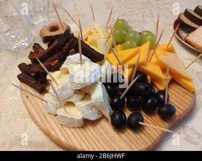 Raccolta di snack con stuzzicadenti su piastra boscosa. Formaggio, olive, pane, uva. Foto Stock
