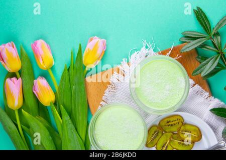 Yogurt di limone alla menta con kiwi in ciotole per insalata su una tavola di legno con tulipani su uno sfondo rosa Foto Stock