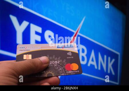 Jaipur India Circa 2020 - una persona vista che tiene una carta di credito, mastercard, da Yes Bank davanti al bordo della banca di sì. Lo sfondo è di colore blu Foto Stock