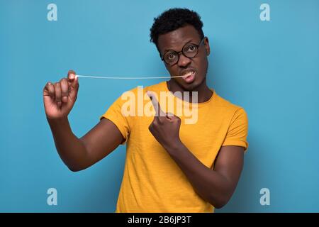Giovane uomo afroamericano in uno studio, tirando una gomma da masticare. Studio girato su parete blu. Foto Stock