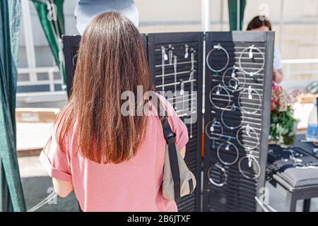 giovane donna con lunghi capelli scuri sceglie bijouterie nel mercato artigianale all'aperto Foto Stock