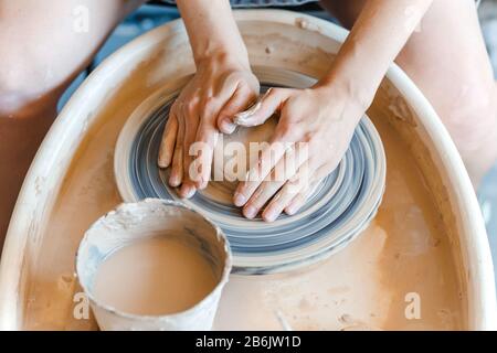 Vista dall'alto delle mani con la produzione di argilla di una pentola in ceramica sul volante, hobby e tempo libero con concetto di piacere Foto Stock