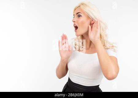 la ragazza chiede di essere più forte mentre tiene la mano vicino all'orecchio su uno sfondo bianco studio Foto Stock