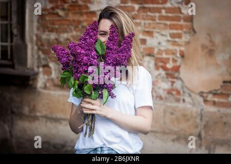 Donna che tiene un mazzo vivido di fiori lilla che nasconde il suo volto. Grunge rosso mattone parete sfondo. Foto Stock