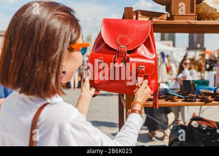 donna in negozio scegliendo borsa e zaino in pelle rossa al mercato all'aperto Foto Stock