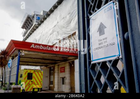 Un cartello NHS punta verso un pod per test Coronavirus, mentre un'ambulanza arriva al DIPARTIMENTO A&e del Kings College Hospital di Camberwell, a sud di Londra, il 11th marzo 2020, a Londra, Inghilterra. Foto Stock