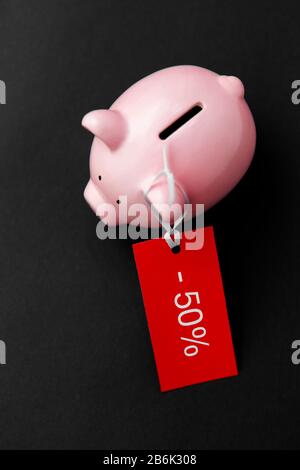 concetto di shopping, vendita e risparmio - banca piggy con etichetta rossa del cinquanta per cento di sconto su sfondo nero Foto Stock