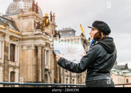 Felice cute giovane donna asiatica in piedi e utilizzando la mappa nella città vecchia europea in autunno o inverno Foto Stock