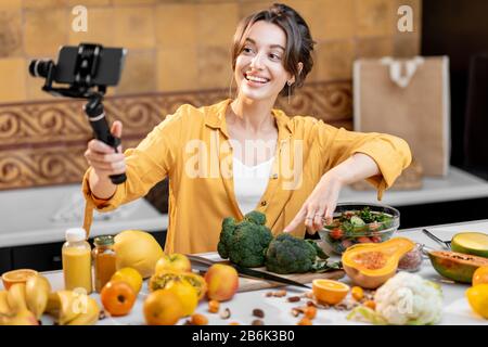 Giovane e allegra donna che vlogging sul telefono cellulare su cibo sano e cucina. Concetto di alimentazione sana e influenza dei social media Foto Stock