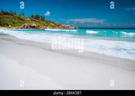 Vacanza. Ondulate onde oceaniche, immacolate laguna di colore blu e rocce di granito sulla spiaggia di Anse Coco, l'Isola di la Digue, Seychelles. Foto Stock