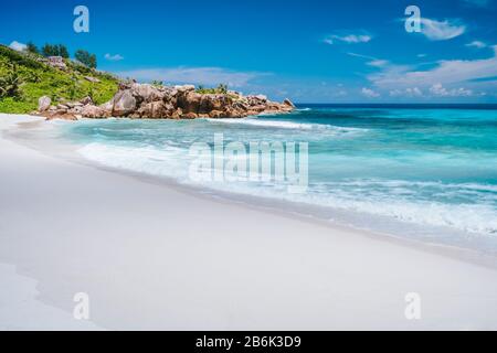 Le onde dell'oceano, la laguna di colore blu incontaminato e le rocce di granito sulla spiaggia di Anse Coco, l'Isola di la Digue, Seychelles. Foto Stock