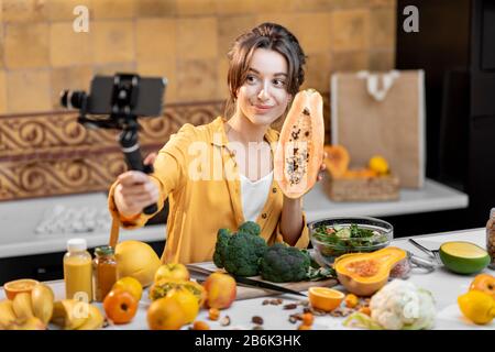 Giovane e allegra donna che vlogging sul telefono cellulare su cibo sano e cucina. Concetto di alimentazione sana e influenza dei social media Foto Stock