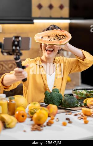 Giovane e allegra donna che vlogging sul telefono cellulare su cibo sano e cucina. Concetto di alimentazione sana e influenza dei social media Foto Stock