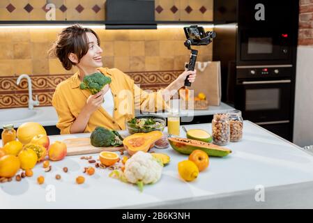 Giovane e allegra donna che vlogging sul telefono cellulare su cibo sano e cucina. Concetto di alimentazione sana e influenza dei social media Foto Stock