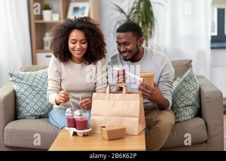 concetto di mangiare e di persone - felice coppia afroamericana con cibo e bevande da asporto a casa Foto Stock