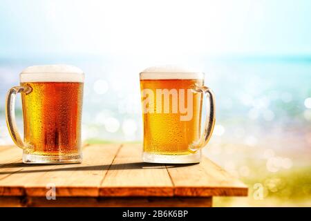 Birra fredda in grande vetro su tavolo di legno con oceano e spiaggia sabbiosa sullo sfondo. Spazio di copia per il prodotto pubblicitario. Foto Stock