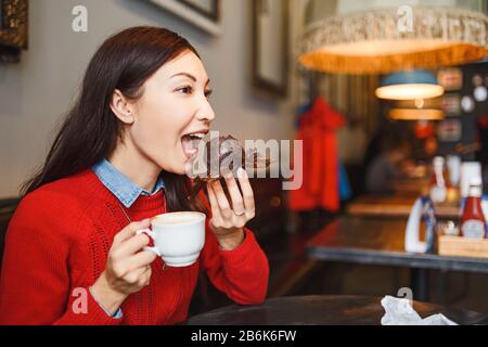 donna bevendo caffè e mangiando una deliziosa torta di muffin nel moderno caffè della città Foto Stock