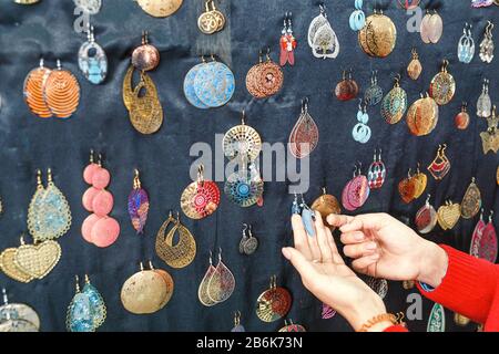 Donna cliente scegliendo tra molti colorati orecchini fatti a mano in vendita alla fiera del mercato Foto Stock