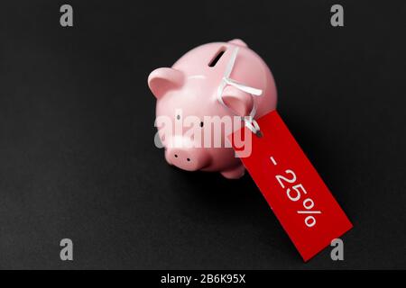 concetto di shopping, vendita e risparmio - banca piggy con etichetta rossa di sconto su sfondo nero Foto Stock