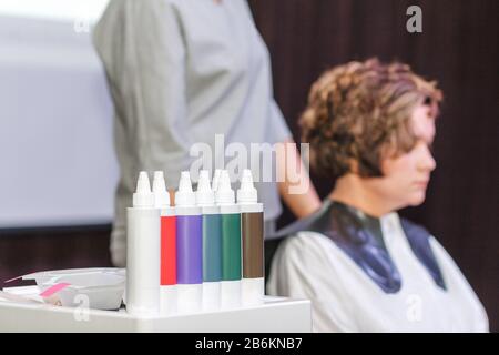 Uno stilista del parrucchiere sta facendo un hairstyle al cliente della donna in un salone di bellezza sullo sfondo di vari prodotti e bottiglie per la cura dei capelli Foto Stock