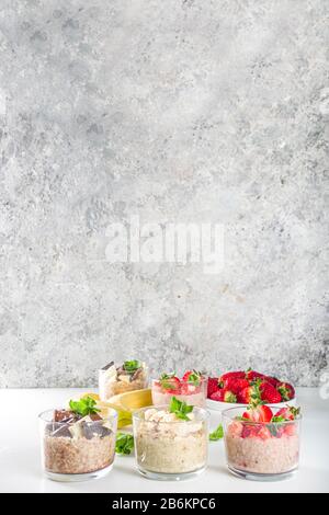 Set vari frutta durante la notte farinata d'avena. Porridge di avena con fragola, banane, cioccolato, noci in piccoli vasi porzione. Colazione estiva con farinata d'avena. Sano Foto Stock