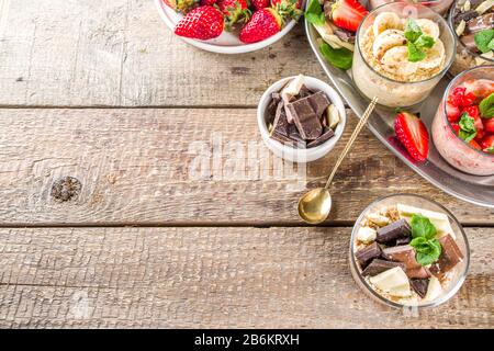 Set vari frutta durante la notte farinata d'avena. Porridge di avena con fragola, banane, cioccolato, noci in piccoli vasi porzione. Colazione estiva con farinata d'avena. Sano Foto Stock