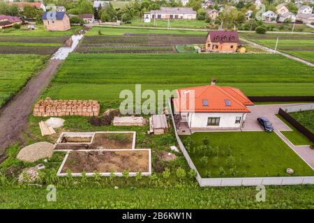 Veduta aerea di una casa privata con finestre soffitta sul tetto, cortile pavimentato con prato verde erba e cantiere con pavimento in cemento e s. Foto Stock