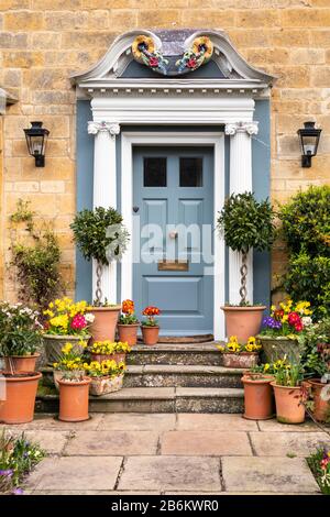 Una mostra di fiori primaverili in vasi fuori di una casa di pietra nel villaggio di Cotswold di Broadway, Worcestershire UK Foto Stock