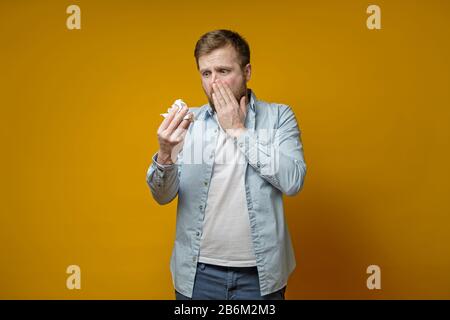 L'uomo caucasico con un naso runny guarda spaventosamente il suo fazzoletto. Concetto di diffusione del virus. Foto Stock
