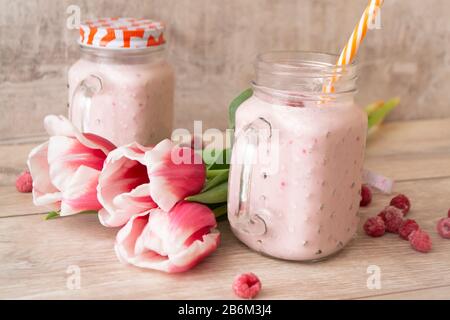 Frullati di proteine di miscela Berry in vaso mason su sfondo chiaro con tulipani fiori, concetto di primavera Foto Stock