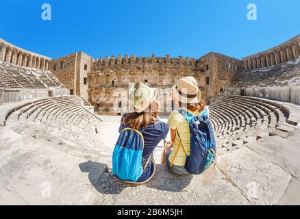 Due giovani ragazze studentesse che viaggiano prendendo selfie l'antico anfiteatro greco Foto Stock