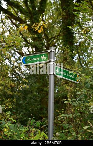 Cartelli per la Bridleway e il sentiero pubblico, su un palo grigio, che puntano in direzioni opposte di fronte agli alberi in un parco di campagna inglese. Foto Stock