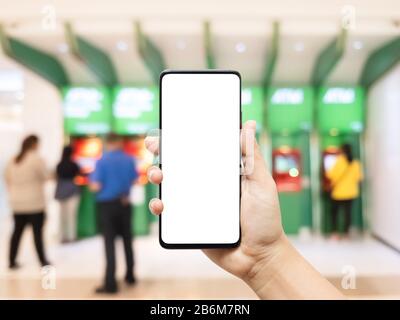 Cellulare mockup, mano utilizzando smartphone con schermo vuoto vuoto con immagine sfocata di persone utilizzando ATM (Automated Teller Machine). Mobile banking, e- Foto Stock
