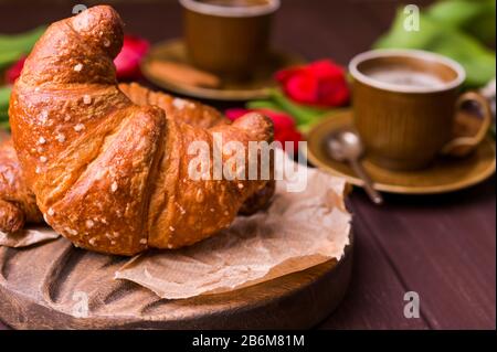 Colazione di Pasqua con caffè espresso fresco aromatico, croissant, uova colorate, tulipani rossi e salice. Caffè con dolci, fiori su un tavolo di legno. Spazio di copia. Foto Stock