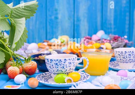 Colazione di Pasqua. Caffè espresso fresco aromatico, succo d'arancia, uova di pasqua su sfondo blu di legno. Spazio di copia Foto Stock