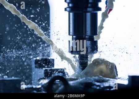 un processo di fresatura verticale dell'acciaio cnc con correnti esterne di liquido di raffreddamento ad acqua, schizzi e un sacco di trucioli metallici, contrasto elevato, profondità di campo poco profonda. Foto Stock