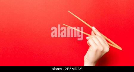 Immagine creativa delle bacchette di legno nelle femmine di mano su sfondo rosso. Il giapponese e il cinese del cibo con copia spazio. Foto Stock
