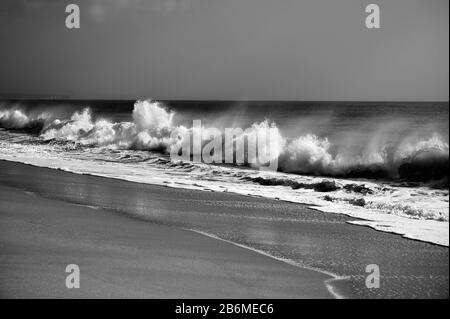 Vento attraverso le onde che si infrangono raggiungono la spiaggia. Fotografia in bianco e nero. Foto Stock