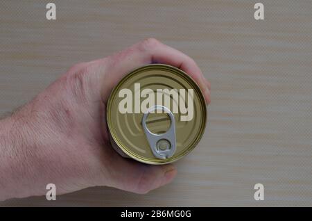 Mano di un uomo adulto tiene una lattina di cibo in scatola. Lattina chiusa con chiave aperta in mano. La mano di un uomo tiene una lattina di cibo in scatola. Cibi in scatola. Questo rea Foto Stock