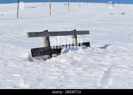 Panca in legno su una montagna coperta di neve profonda. Foto Stock