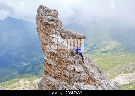 Donna in via ferrata Cesare Piazzetta, in piedi su una roccia pointosa sopra la strada tortuosa al passo di Pordoi, montagne dolomitiche, Italia. Concetto per l'estate Foto Stock