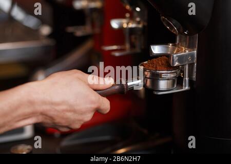 Macinacaffè professionale per macinare chicchi di caffè arrostiti freschi. Barista che tiene il portafiltro senza fondo con caffè macinato. Caffè da caffè. Cof Foto Stock
