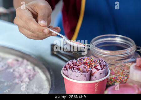 La preparazione di gelato, cibo di strada tailandese, cucinare cosparge di gelato in una tazza di carta con caramello. Foto Stock