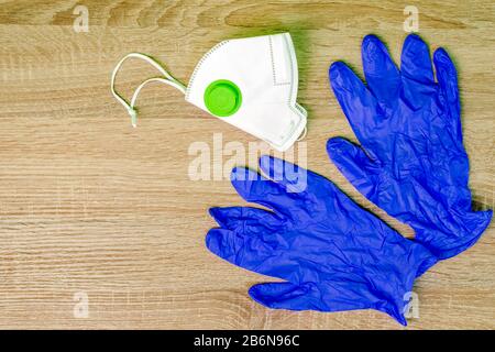 Guanti medici in gomma blu e maschera respiratoria si trovano su un tavolo in legno. Concetto di igiene e protezione dell'uomo dai batteri. Copiare lo spazio per il testo. In Alto Foto Stock